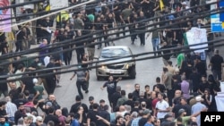 People react around a car after a reported explosion occurred during the funeral of those killed when hundreds of paging devices exploded across Lebanon the previous day, in Beirut's southern suburbs, Sept. 18, 2024.