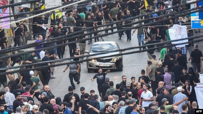 People react around a car after a reported explosion occurred during the funeral of those killed when hundreds of paging devices exploded across Lebanon the previous day, in Beirut's southern suburbs, Sept. 18, 2024.