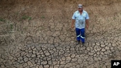 FILE - A farmer stands on cracked earth on his farm in Groot Marico, South Africa, Nov. 12, 2015.