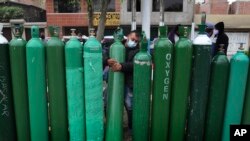 Edgar Barbaran exchanges a small, empty oxygen tank for a large one as he waits since the previous day for a refill shop to open in Callao, Peru, amid the COVID-19 pandemic.