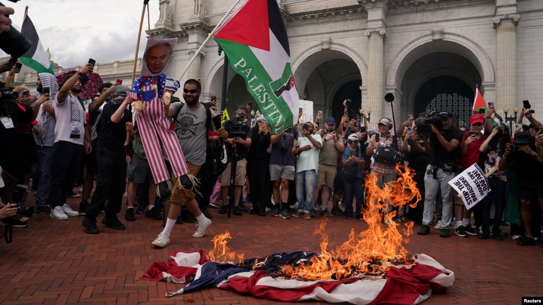 Bendera AS dibakar sementara seorang demonstran pro-Palestina memegang patung Perdana Menteri Israel Benjamin Netanyahu, selama aksi protes anti-Netanyahu di luar Union Station di Washington, DC hari Rabu (24/7). 