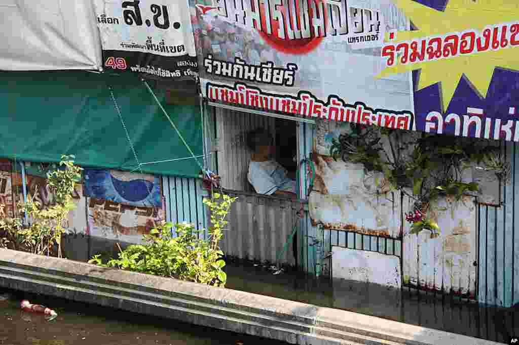 A man rests in his shop surrounded by floodwaters in Bangkok, October 27, 2011. (VOA - D. Schearf)