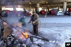 A man warms his hands by the fire he created across the street from a homeless encampment under a major interstate freeway Tuesday, Jan. 16, 2024, in Chicago. Scientists say that climate change is causing extreme temperatures around the world. (AP Photo/Charles Rex Arbogast)