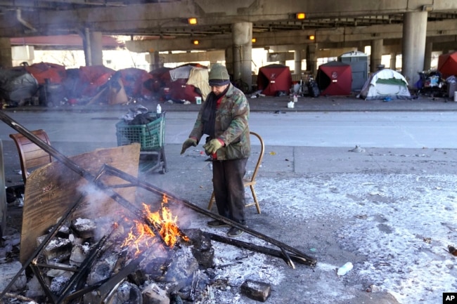 A man warms his hands by the fire he created across the street from a homeless encampment under a major interstate freeway Tuesday, Jan. 16, 2024, in Chicago. Scientists say that climate change is causing extreme temperatures around the world. (AP Photo/Charles Rex Arbogast)