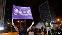A demonstrator holds up a sign reading "Back away slowly" to encourage other demonstrators to leave, near the Chinese Liaison Office in Hong Kong, Sunday, Aug. 18, 2019. 