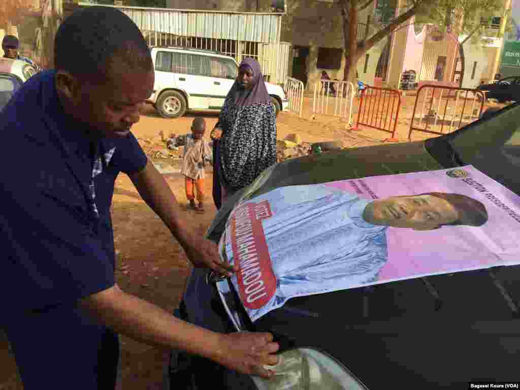 Un supporter du président sortant pose une de ses affiches sur son véhicule, Niamey, 15 mardi 2016. (VOA/Bagassi Koura)