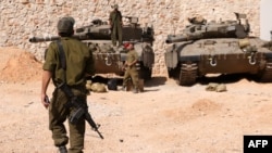 FILE - Israeli soldiers gather near Merkava tanks as they man a position at an undisclosed location on the border with Lebanon on October 22, 2023.