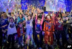 In this photo provided by NASA, a NASA scientist celebrates with school children at the exact moment that the New Horizons spacecraft made the closest approach of Kuiper Belt object Ultima Thule, Jan. 1, 2019.