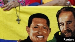 Một người ủng hộ Tổng thống Chavez cầm chiếc Thánh giá cạnh bức ảnh của ông và nhà cựu lãnh đạo Cuba, Fidel Castro (phải), 5/1/13