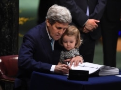 FILE - Then-U.S. Secretary of State John Kerry holding his granddaughter, Isabelle Dobbs-Higginson, signs the book during the signature ceremony for the Paris Agreement at the United Nations General Assembly Hall, April 22, 2016, in New York.