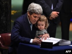 FILE - Then-U.S. Secretary of State John Kerry holding his granddaughter, Isabelle Dobbs-Higginson, signs the book during the signature ceremony for the Paris Agreement at the United Nations General Assembly Hall, April 22, 2016, in New York.