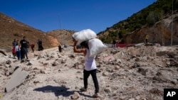 Orang-orang membawa barang bawaan mereka untuk menyeberang ke Suriah, melalui lubang yang ditimbulkan dari serangan udara Israel untuk memblokir jalan raya Beirut-Damaskus di penyeberangan Masnaa di timur Bekaa Valley, Lebanon, Sabtu, 5 Oktober 2024. (Foto: Hassan Ammar/AP Photo)