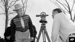 Philip N. Brooks, right, a New York State surveyor, takes a look through his transit on the Tuscarora Indian Reservation near Niagara Falls, N.Y., while Tuscarora Chief Elton Black Cloud Greene looks back at him, April 18, 1958. (AP Photo)