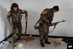 FILE - An Arab fighter, left, and Kurdish fighter with the SDF hold their weapons as they prepare to battle Islamic State militants, in Raqqa, northeast Syria, July 22, 2017.