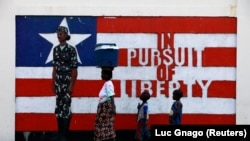 FILE - A woman and two children walk past a mural in Monrovia, Liberia, Nov. 10, 2011. The United Nations on Wednesday lifted the last international sanctions against Liberia. 