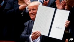 El presidente Donald Trump sostiene una orden ejecutiva firmada para aliviar una regla del IRS que limita la actividad política de las iglesias, el jueves 4 de mayo de 2017, en el Jardín de las Rosas de la Casa Blanca en Washington.