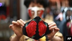 In this Wednesday, April 15, 2020, photo, fashion designer Do Quyen Hoa shows off an embroidery face mask at her studio in Hanoi, Vietnam. The collection of face masks adorned with Vietnamese hand embroideries was created as the world is fighting against 