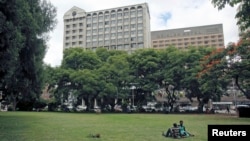 FILE - Zimbabweans rest at a park outside Meikles Hotel in central in Harare, February 24, 2015.