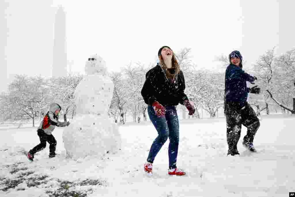 Dane Lariscy, 5, left, works on a snowman as his siblings, Amanda Lariscy, 17, and Blaze Lariscy, 15, are having a snowball fight on the National Mall during a spring snowstorm in Washington, D.C.