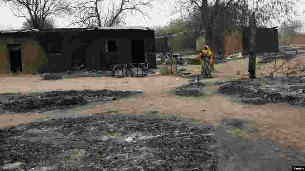 A woman carrying a child stands near burnt houses in the aftermath of what Nigerian authorities said was heavy fighting between security forces and Islamist militants in Baga