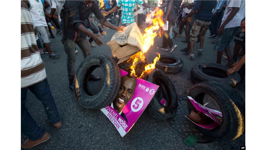 Supporters of presidential candidate Maryse Narcisse, from the Fanmi Lavalas political party, burn tires and a campaign poster of rival candidate Jovenel Moise, from the PHTK party, in Port-au-Prince, Haiti, Nov. 28, 2016.