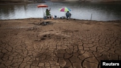 FILE - Men fish next to cracked ground as the Atibainha dam lake dries up due to a prolonged drought in Nazare Paulista, Sao Paulo state, Brazil, Oct. 17, 2014. 