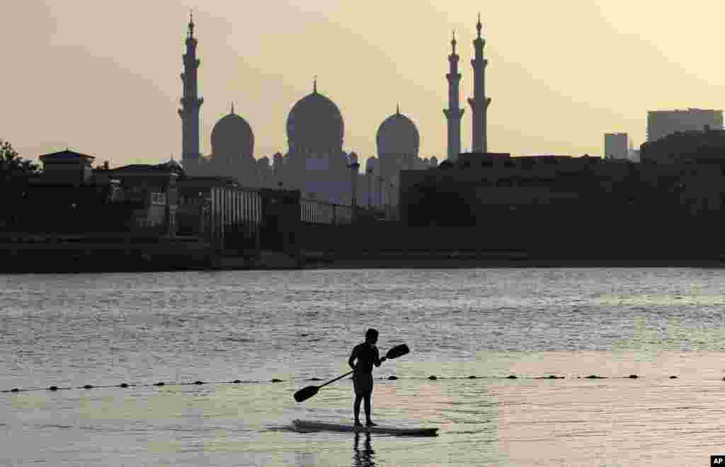 A surfer paddles in front of the Sheikh Zayed Grand Mosque in Abu Dhabi, United Arab Emirates.