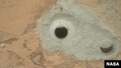 Na jednoj od fotografija koju je Kjuriositi poslao NASI na zemlju vidi se stena poznata kao Džon Klajn sa koje je rover uzeo prve uzorke tla Marsa. 