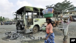 Women carrying loads on their heads walk past a burnt-out bus in Abobo, an Alassane Ouattara stronghold in Abidjan, February 8, 2011