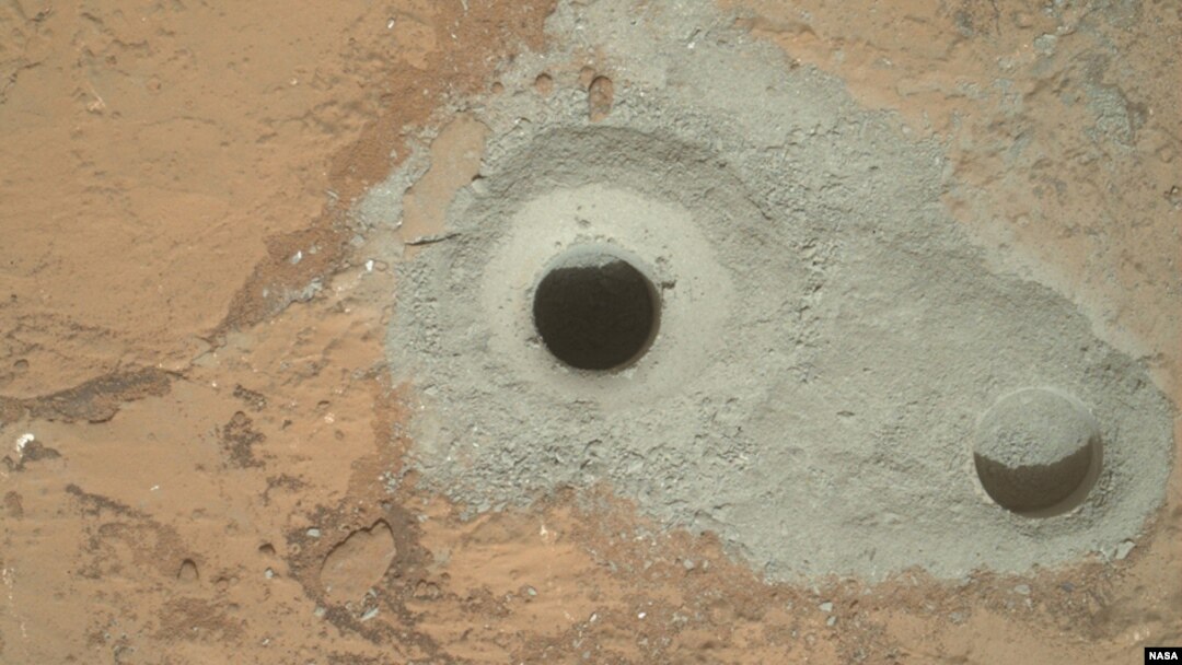 Na jednoj od fotografija koju je Kjuriositi poslao NASI na zemlju vidi se stena poznata kao Džon Klajn sa koje je rover uzeo prve uzorke tla Marsa. 