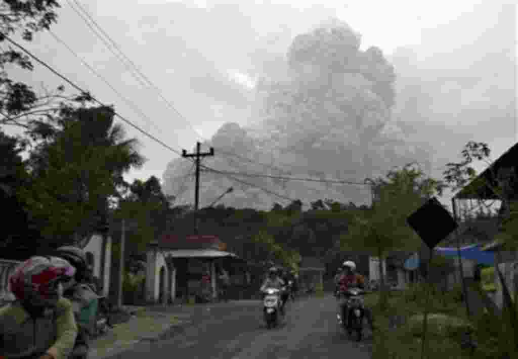 Motorists ride as pyroclastic material from the eruption of Mount Merapi billows in the background in Cangkringan, Yogyakarta, Indonesia,31 Oct 2010