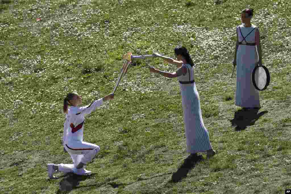 Greek actress Xanthi Georgiou, center, playing the role of the High Priestess, lights the torch of the 2020 Tokyo Olympic Games, held by Greek shooting Olympic champion Anna Korakaki, left, the first torchbearer, during the flame lighting ceremony at the closed Ancient Olympia site in southern Greece.