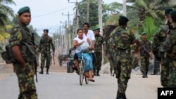 A Sri Lankan resident rides a bicycle along a road as Special Task Force (STF) soldiers patrol following clashes between Muslims and an extremist Buddhist group in the town of Alutgama, June 16, 2014.