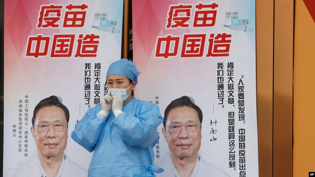 资料照：一名医护人员站在中国疫苗的广告前。（2021年4月9日）(photo:VOA)