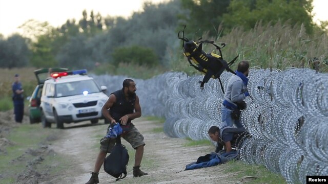 Policías húngaros observan a migrantes sirios ingresando ilegalmente por una cerca en la frontera entre Hungría y Serbia