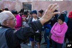A volunteer who helped with the delivery of a donated breakfast prays as Central American migrants wait in a line to receive the breakfast at a temporary shelter in Tijuana, Mexico, Nov. 17, 2018. The mayor has called the migrants' arrival an "avalanche" that the city is ill-prepared to handle.