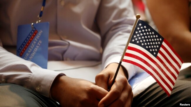 一名新公民在纽约公共图书馆的公民宣誓仪式上手持美国国旗（2018年7月3日）