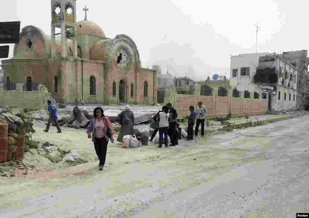 Residents walk near a damaged church in Qusair, Syria, June 8, 2013.