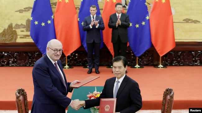 欧盟农业和农业发展事务专员菲尔·霍甘与中国商务部长钟山在北京人大会堂签署协议。中国国家领导人习近平和法国总统马克龙站在后方。（2019年11月6日）