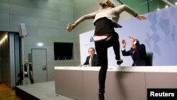 A protester jumps on the table in front of the European Central Bank President Mario Draghi during a news conference in Frankfurt, April 15, 2015. The news conference was disrupted on Wednesday when a woman in a black T-shirt jumped on the podium. REUTERS