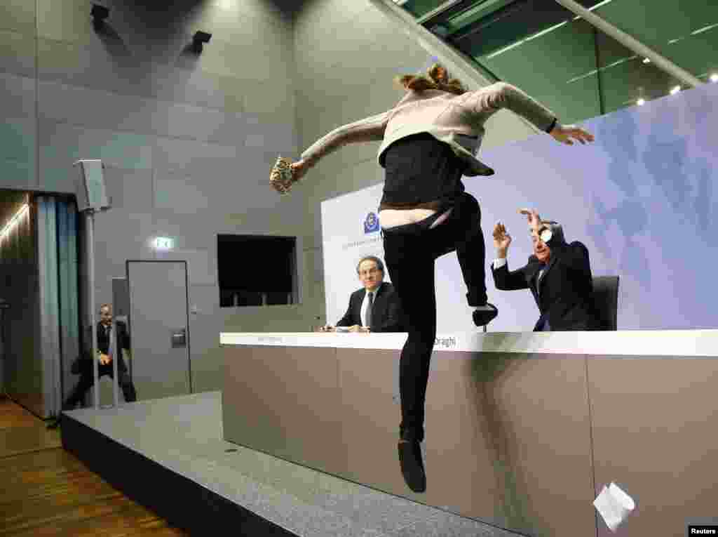 A protester jumps on the table in front of the European Central Bank President Mario Draghi during a news conference in Frankfurt, Germany.