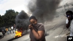 A woman covers her face from the smoke of burning tires set up by demonstrators in Port-au-Prince, Haiti, 15 Nov. 2010.