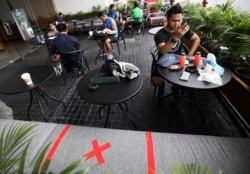 Para pengunjung sebuah kafe di Gelora Bung Karno duduk dalam jarak tertentu dalam upaya mencegah penyebaran virus corona, Jakarta, 26 Maret 2020. (Foto: Dita Alangkara/AP)