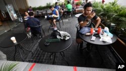 Para pengunjung sebuah kafe di Gelora Bung Karno duduk dalam jarak tertentu dalam upaya mencegah penyebaran virus corona, Jakarta, 26 Maret 2020. (Foto: Dita Alangkara/AP)