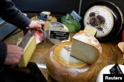 FILE - A cheesemonger cuts a large piece of Comte cheese at Beaufils affineur in Paris as France celebrates national Fromage day to protect real raw milk cheese, France, March 27, 2019. (REUTERS/Charles Platiau)