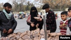 An Afghan woman buys food left behind by the U.S. military from a peddler in Kabul, Afghanistan on Nov. 17, 2021