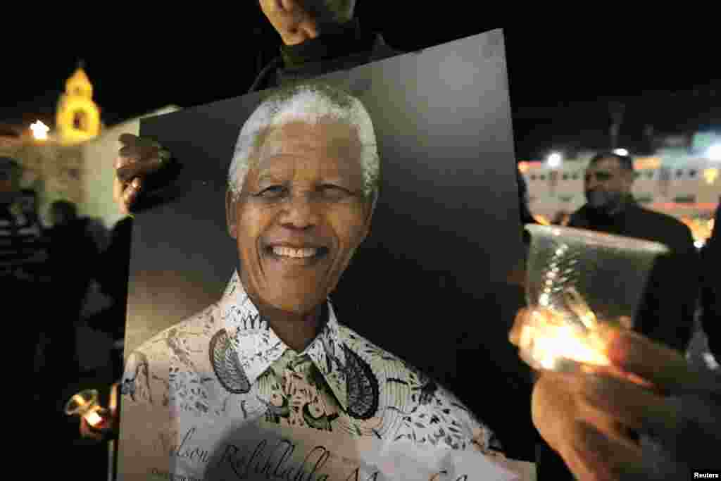 Palestinians light candles and hold placards bearing images of former South African President Nelson Mandela outside the Church of Nativity in the West Bank town of Bethlehem December 7, 2013. South African anti-apartheid hero Mandela died peacefully at h