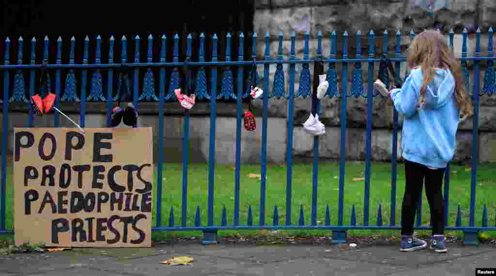 A girl ties baby shoes to a fence as a part of a protest to highlight child abuse at the hands of the Catholic church, during the visit of Pope Francis to Dublin, Ireland.