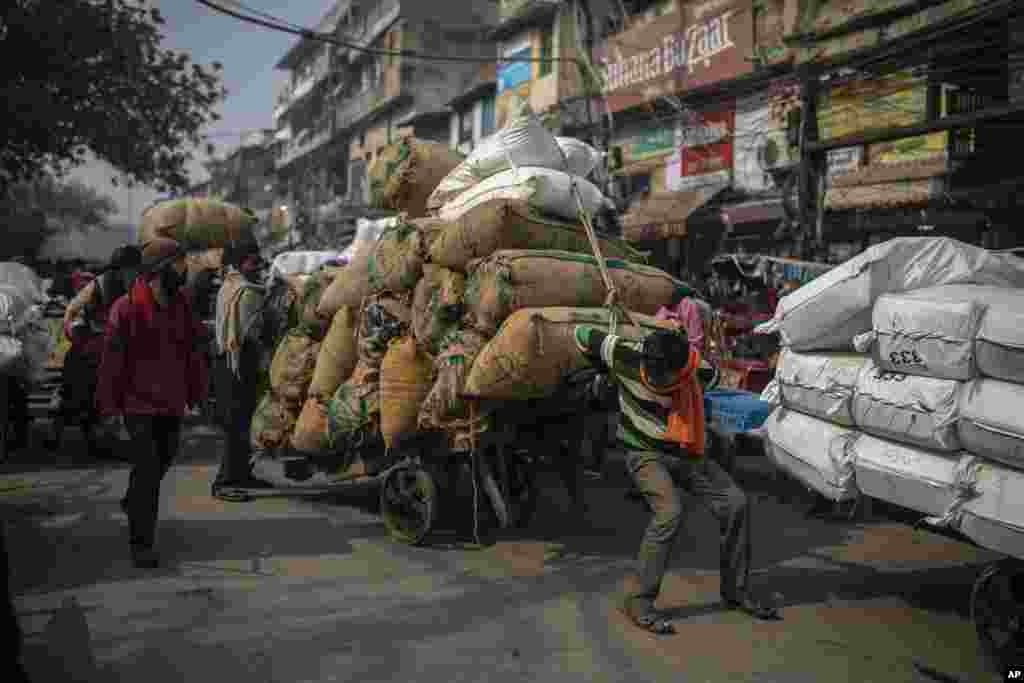 Seorang buruh berusaha mengendalikan gerobaknya yang penuh muatan, melalui sebuah pasar yang padat di New Delhi, India, Selasa, 1 Februari 2022. (Foto: AP)