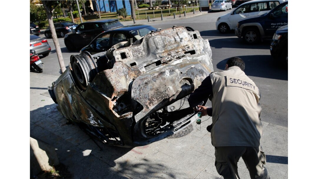 A private security worker photgraphs a car burned by supporters of the Shiite Hezbollah and Amal groups in Beirut, Dec. 17, 2019. The groups were angered by a video that showed a man insulting Shiite figures.